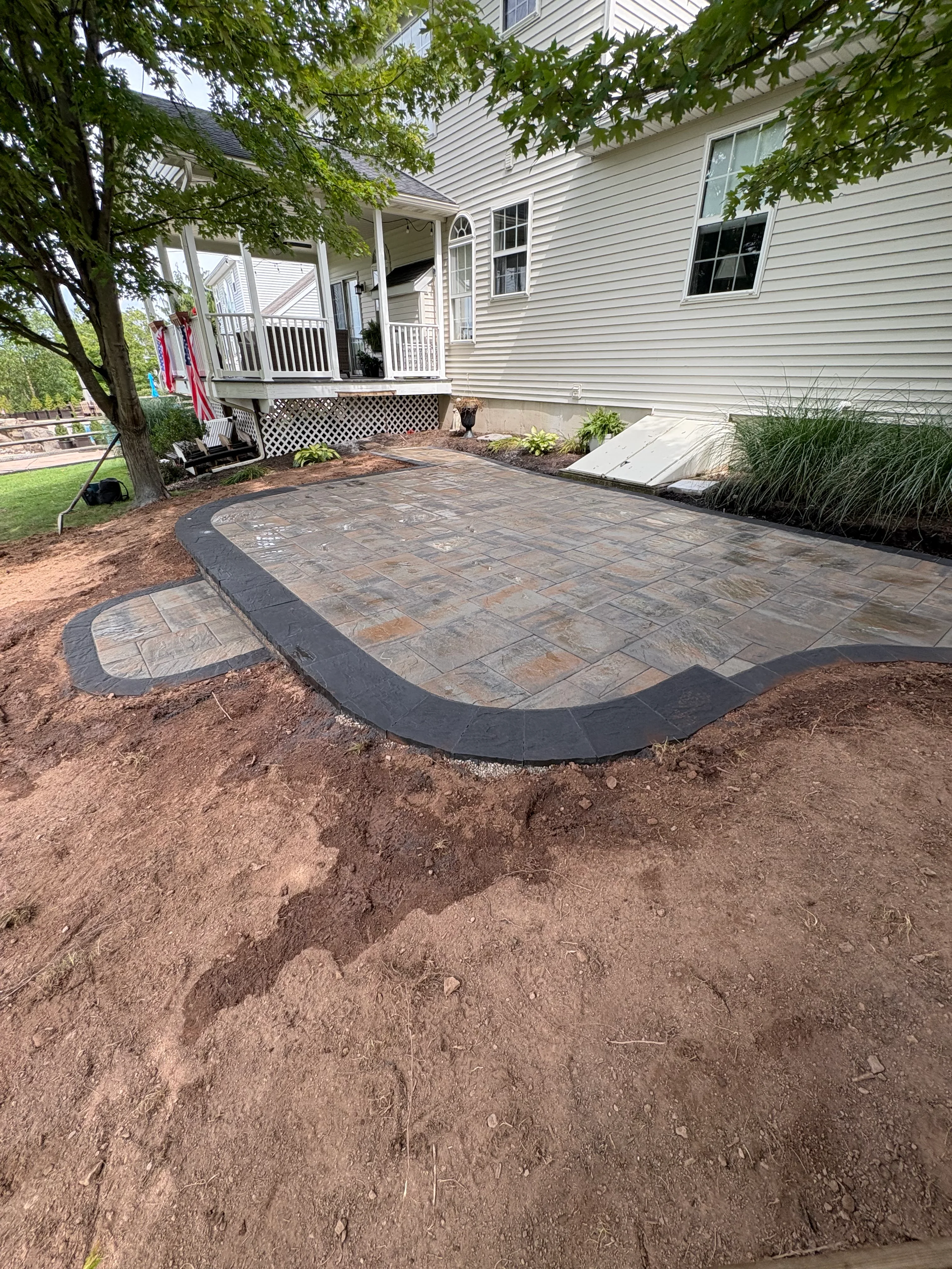 Newly installed paver patio with curved dark border, tumbled stone pavers, and landscape edging