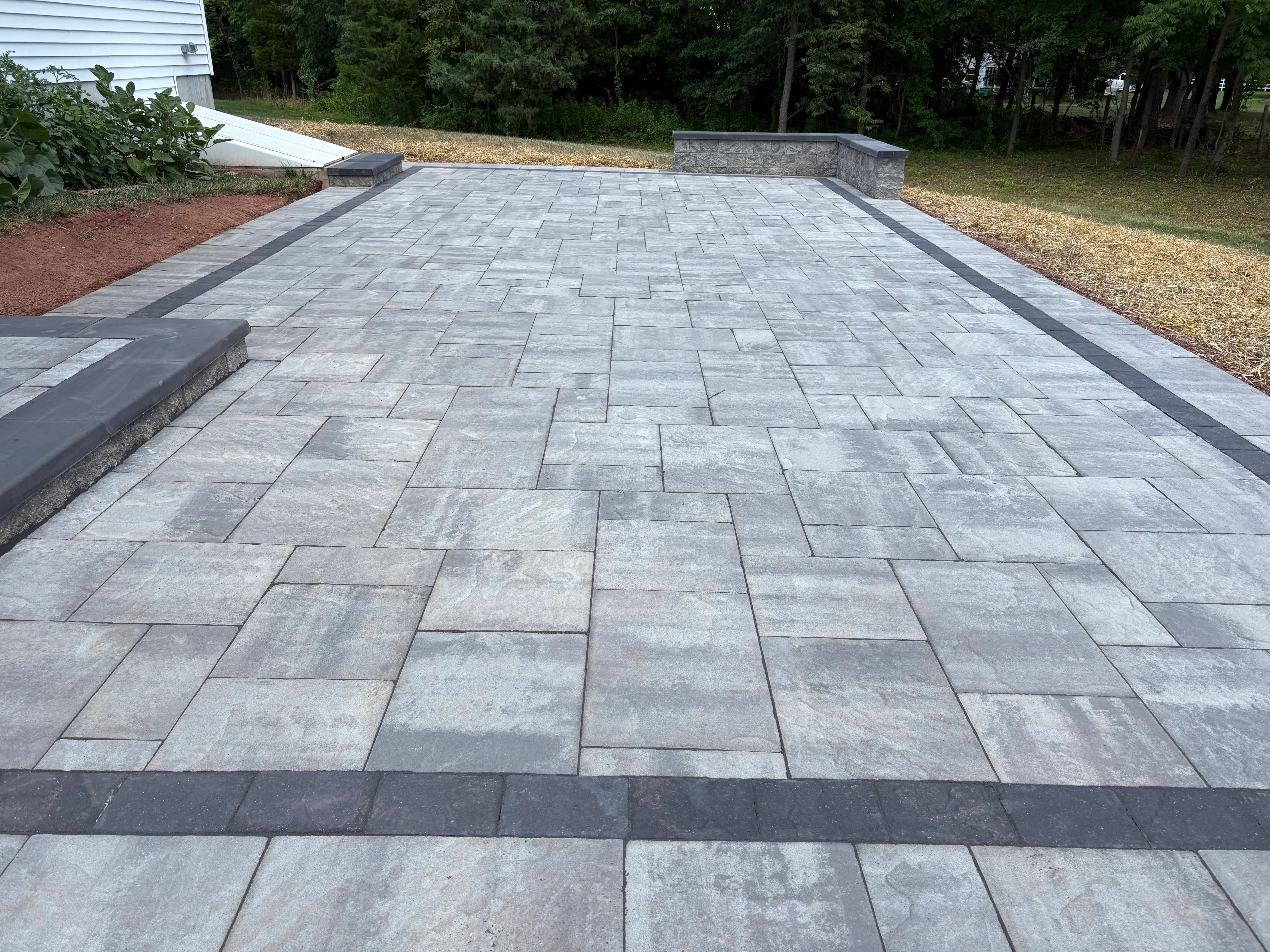 Gray concrete paver patio with dark border and retaining wall in herringbone pattern