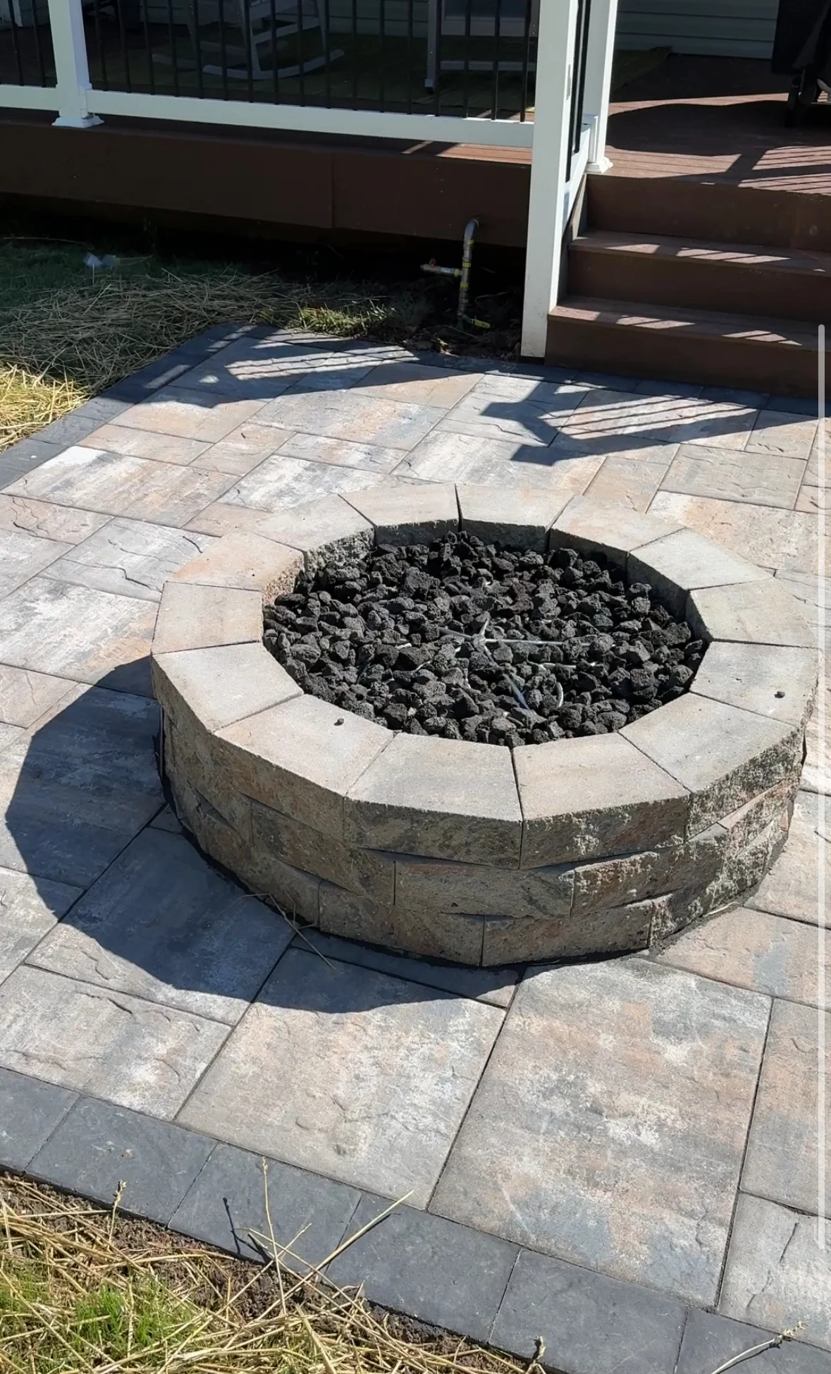 Circular stone fire pit with lava rock fill on paver patio with running bond pattern